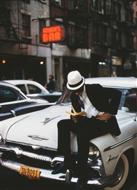 Man with white Hat reading on a car, 1952